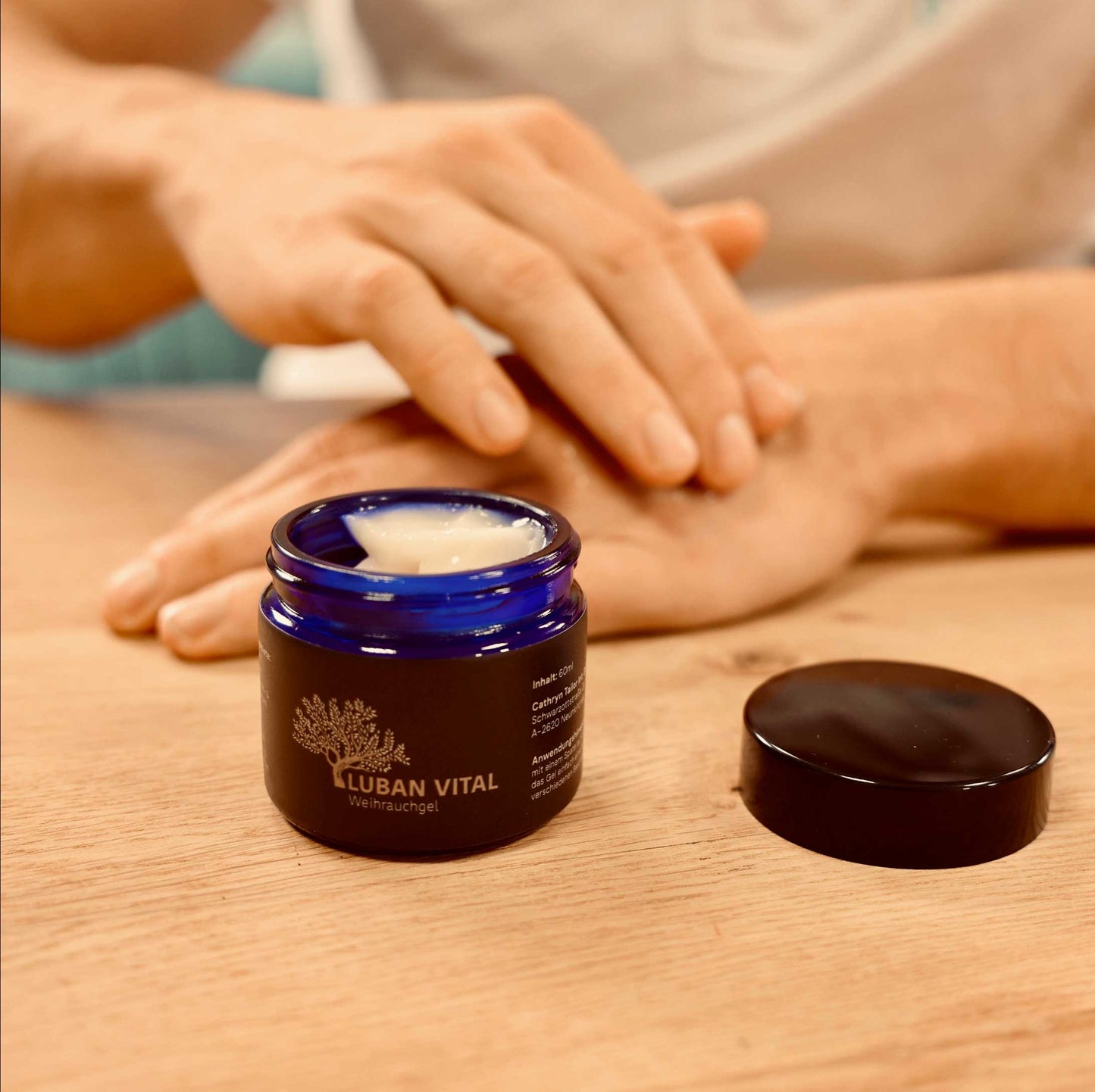 Hand entnimmt Creme aus einem blauen Glas-Tiegel Luban Vital Weihrauchgel